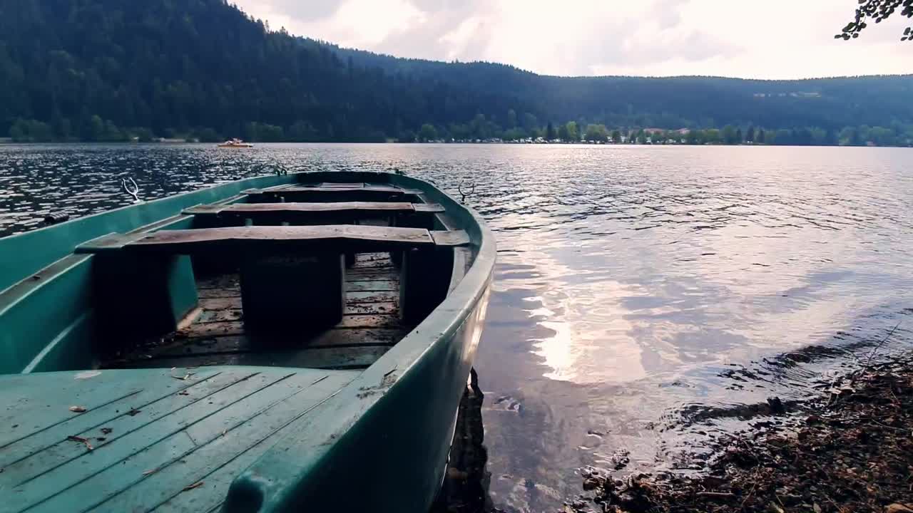 un pequeño barco pesquero está estacionado en la playa frente a un hermoso lago en francia