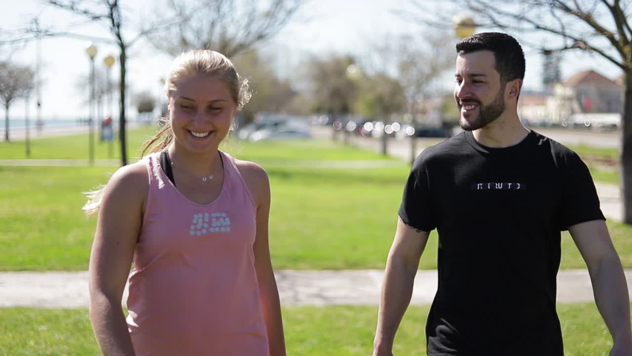 una joven pareja sonriente y deportiva caminando por el parque y hablando.