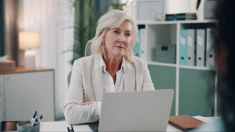 a businesswoman sits at her desk in an office and talks during a video conference.