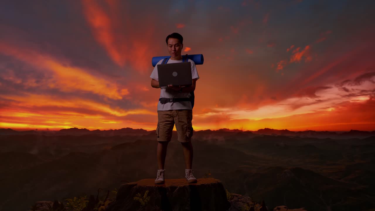 hombre feliz trabajando en una computadora portátil en la cima de la montaña al atardecer
