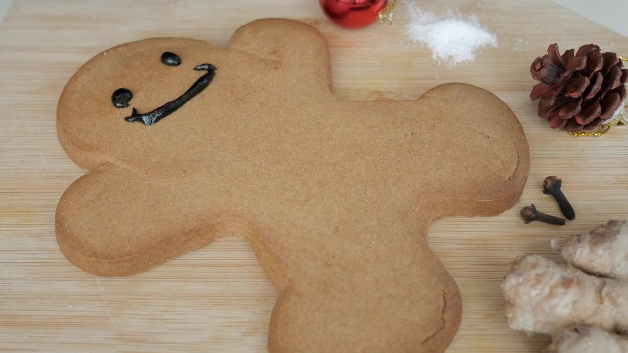 Blank large gingerbread cookie on wooden board being decorated with coloured icing. Spices and seasonal decoration nearby