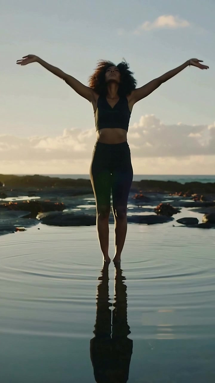 Video verticale: Donna con top sportivo che si solleva facendo stretching sopra la testa da una posa in una pozza di marea.