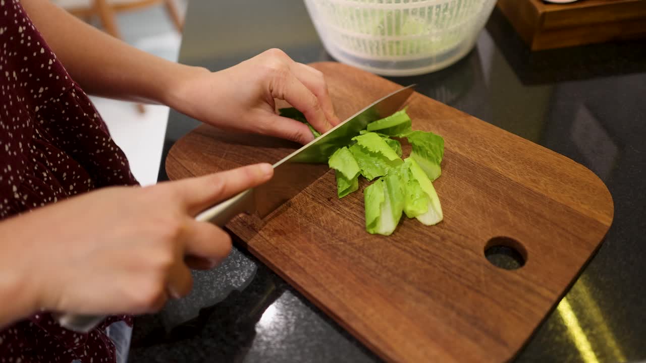 A chef uses a sharp knife to chop fresh green lettuce on a wooden board