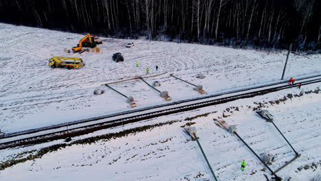 Hombres-Y-Equipos-Trabajando-En-La-Instalación-De-Postes-De-Servicios-Públicos-Y-Cables-Eléctricos-A-Lo-Largo-Del-Ferrocarril-En-Un-Paisaje-Nevado-En-Invierno