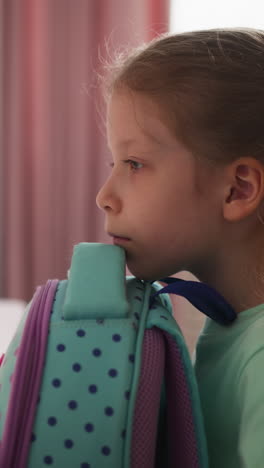 pretty girl pupil opens rucksack and looks inside sitting at desk in classroom. calm schoolgirl seeks supplies in large backpack at table in class