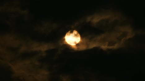 yellow moon or sun seen through dark clouds with birds quickly flying in front