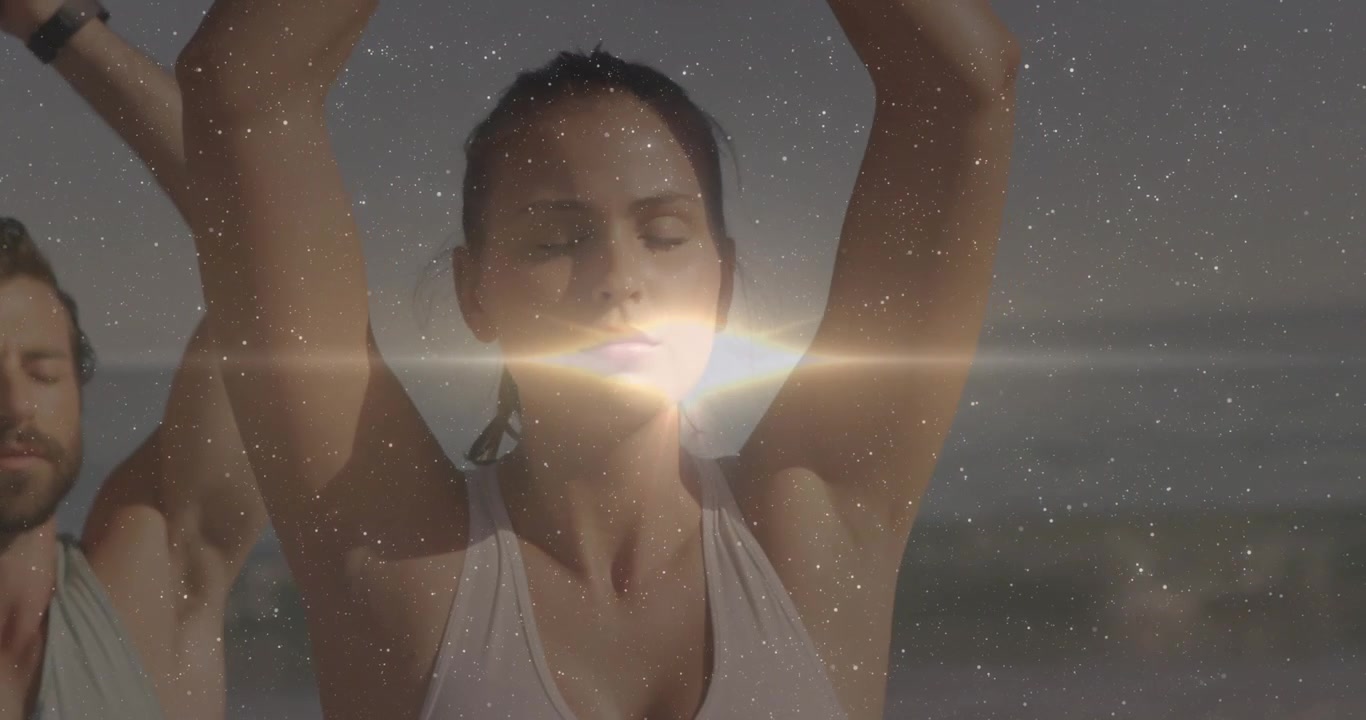 Grupo siguiendo una instrucción en la playa manteniendo una postura de yoga para bienestar mientras un destello de luz se extiende por sus caras.