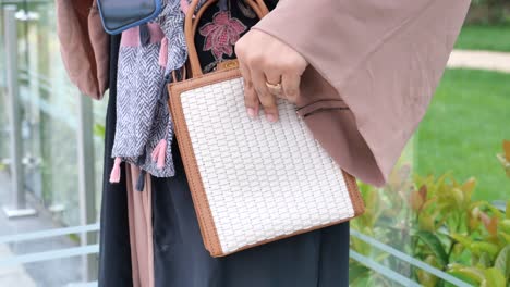 a woman wearing a hijab and abaya holds a handbag