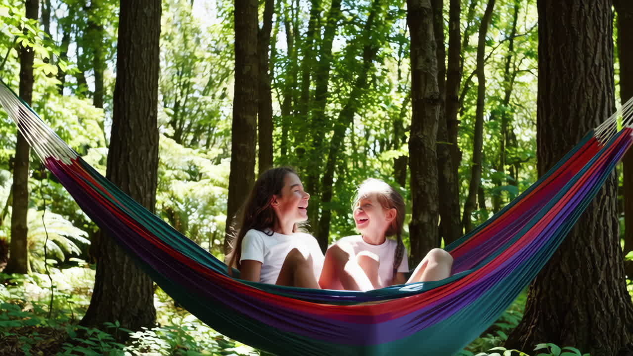 Two happy girls laughing in a colorful hammock in a forest