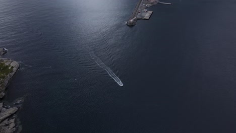 top tracking view of motorboat entering reinevagen bay waters passing reine lighthouse - orbiting aerial shot, norway