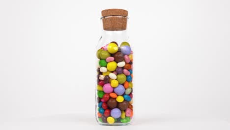 variety of colored candies rotate in a transparent bottle on white background. isolated. loopable.