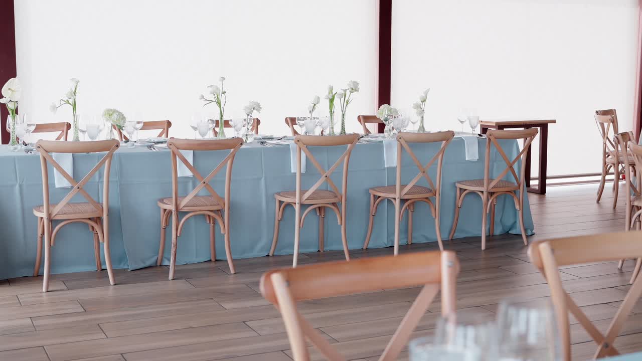long table set for event with blue cloth and wooden chairs in bright space