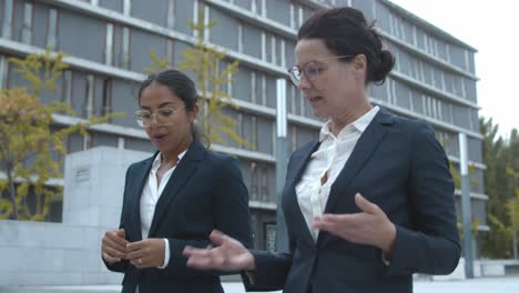 two confident business women talking together while walking near office building