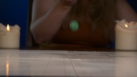 mujer tira un dado verde de veinte caras sobre una mesa de juego con velas encendidas