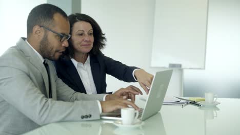 empleados de la oficina alegres sentados en la mesa y usando la computadora portátil