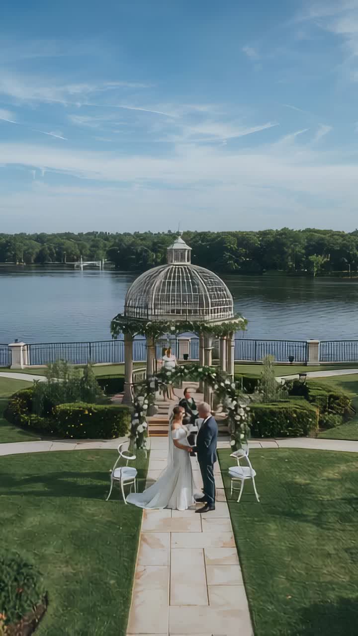 Vertical video: Officiant reading book, bride gown groom suit exchanging vows under lakeside arch