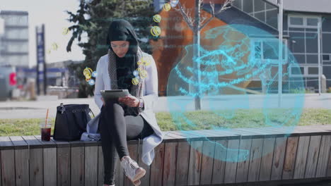 globo y múltiples iconos digitales flotando sobre una mujer en hijab usando una tableta digital en la calle