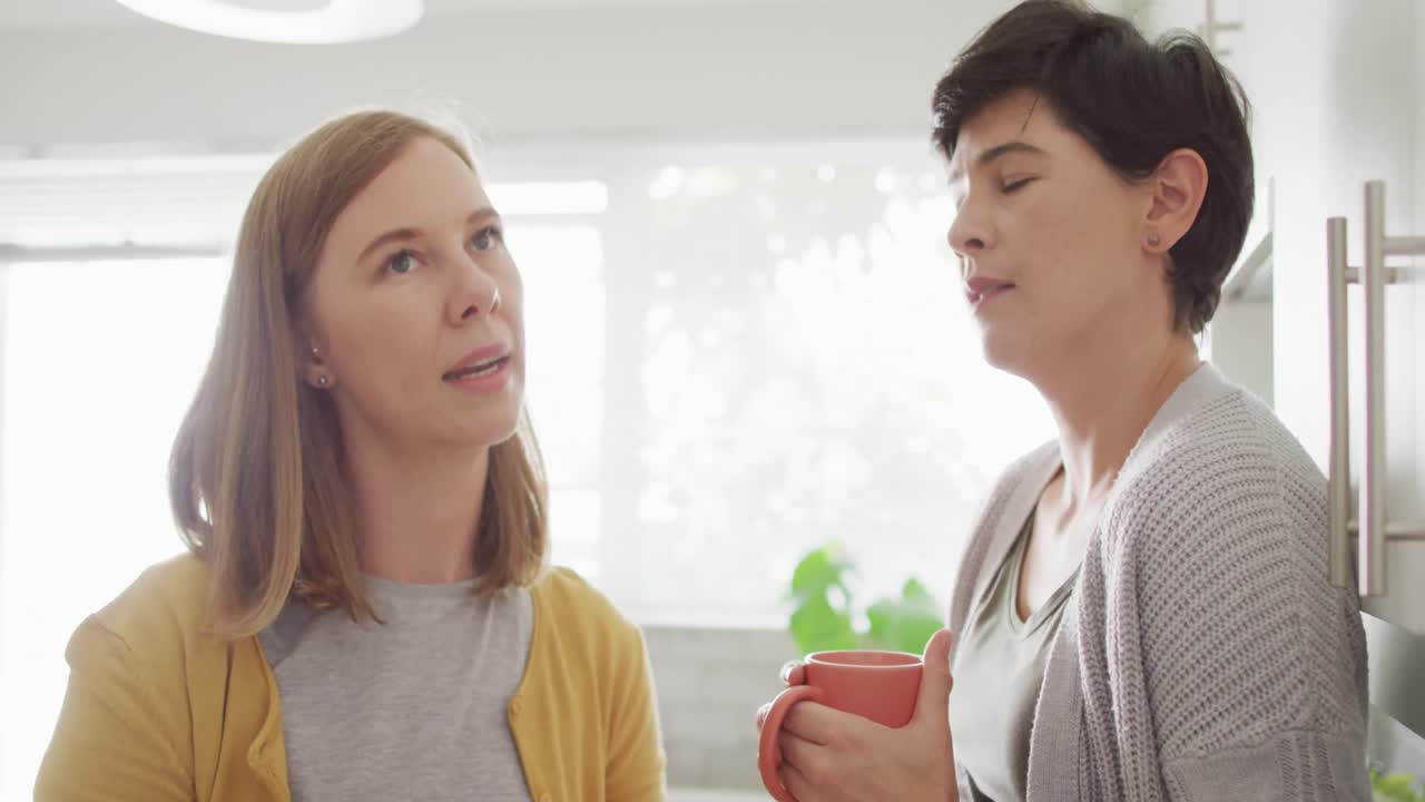 카우카시안 레즈비언 커플 이 집 의 주방 에서 커피 를 마시면서 서로 이야기 하고 있다