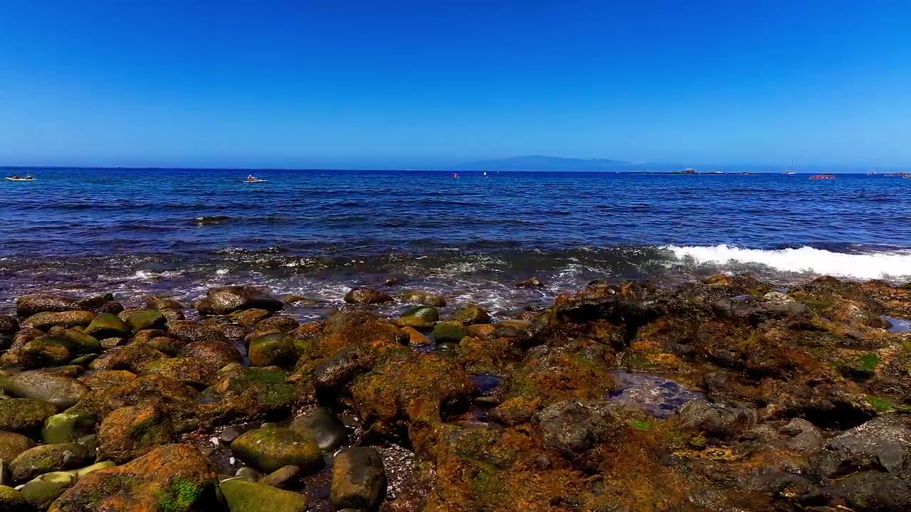Naturskøn lavvinkeludsigt over havbølger, der bryder mod den klippefyldte kystlinje og vegetationen ved Punta del Bocinegro på Tenerife, De Kanariske Øer.