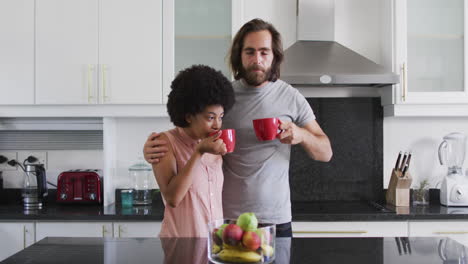 biracial couple drinking coffee together in the kitchen at home