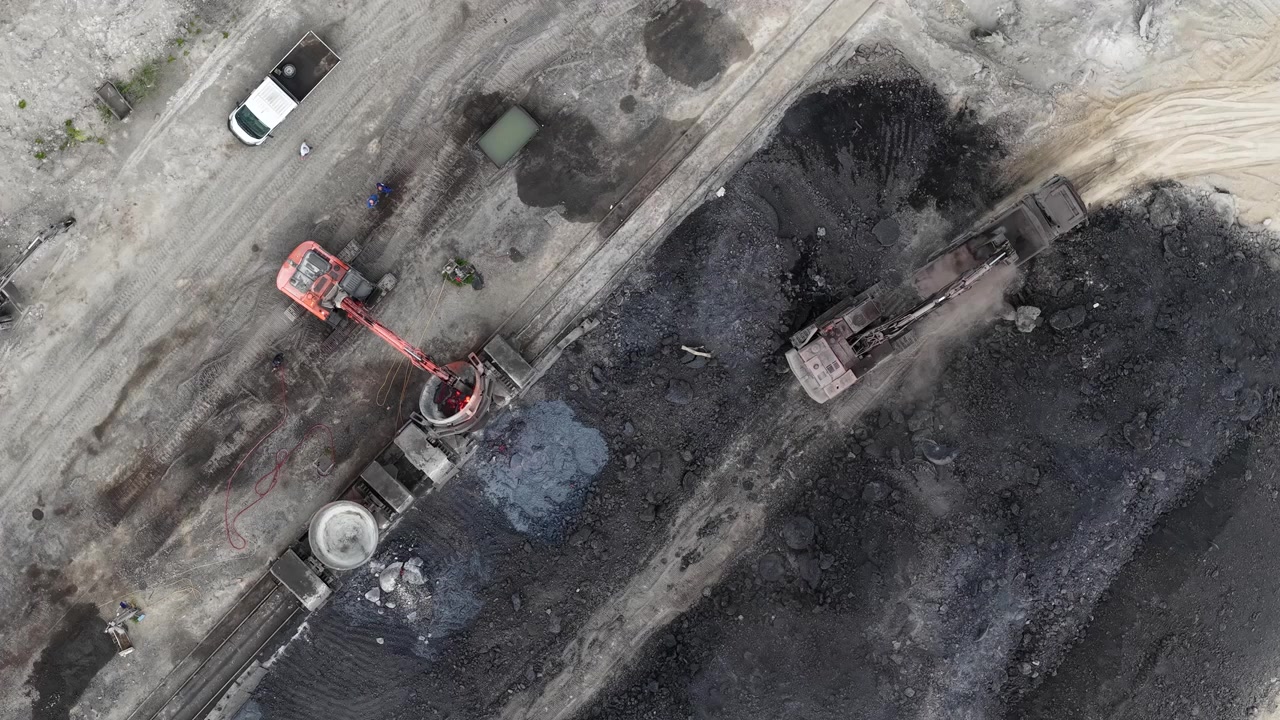 An aerial view reveals excavators loading raw coal at a dusty industrial site, highlighting heavy industry and essential energy resource extraction in Hungary.