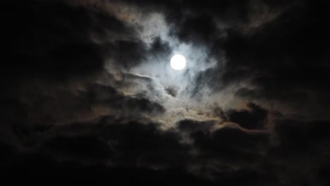 slow time lapse of stationary full moon with halo behind clouds, copy space