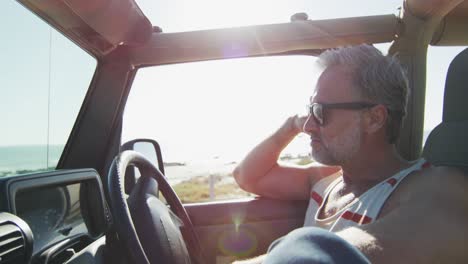 Thoughtful-caucasian-man-in-sunglasses-sitting-in-car-on-sunny-day-by-the-sea