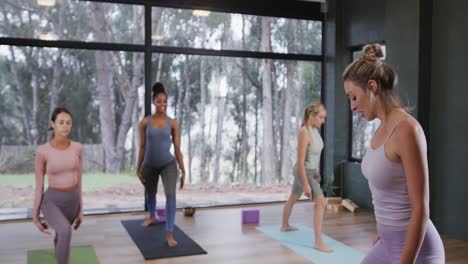 mujeres diversas estirándose juntas en esteras en la clase de yoga con una entrenadora femenina, cámara lenta