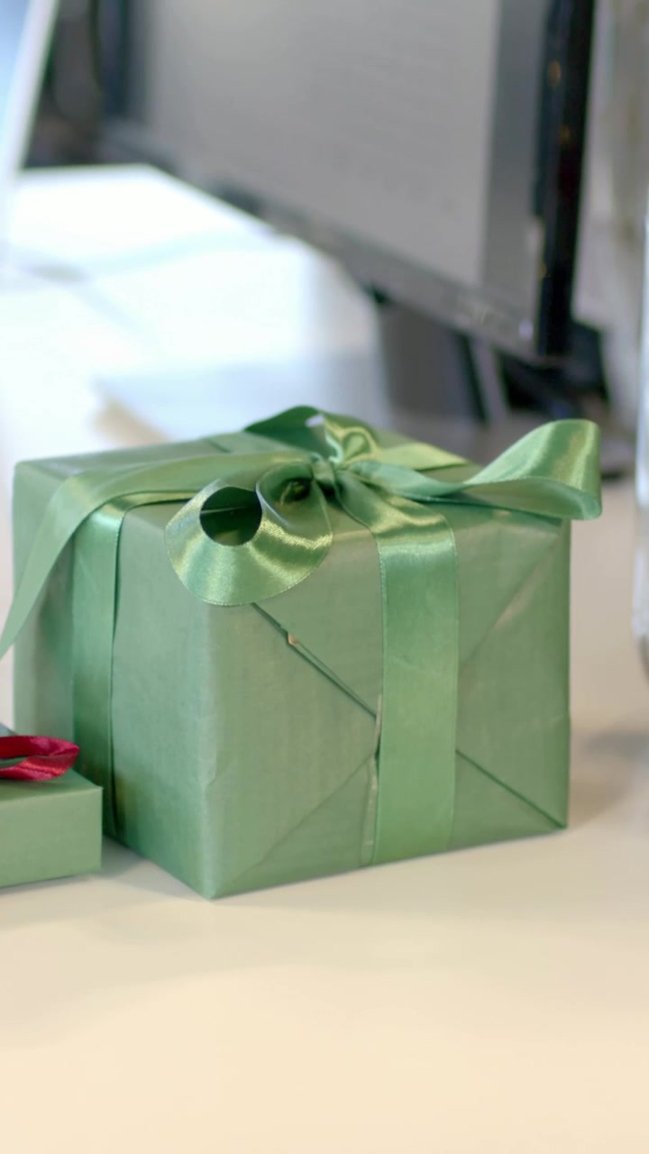 Video verticale: Telecamera che si sposta e zooma, inquadrando una scatola regalo verde sulla scrivania e mettendo a fuoco il fiocco.