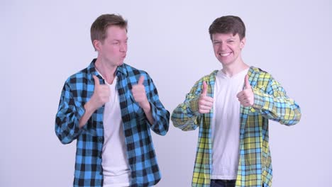 two happy young handsome men giving thumbs up together