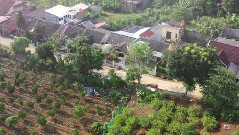 Motorbikes-driving-through-a-local-village-with-farmland-in-Bandung-Indonesia,-aerial