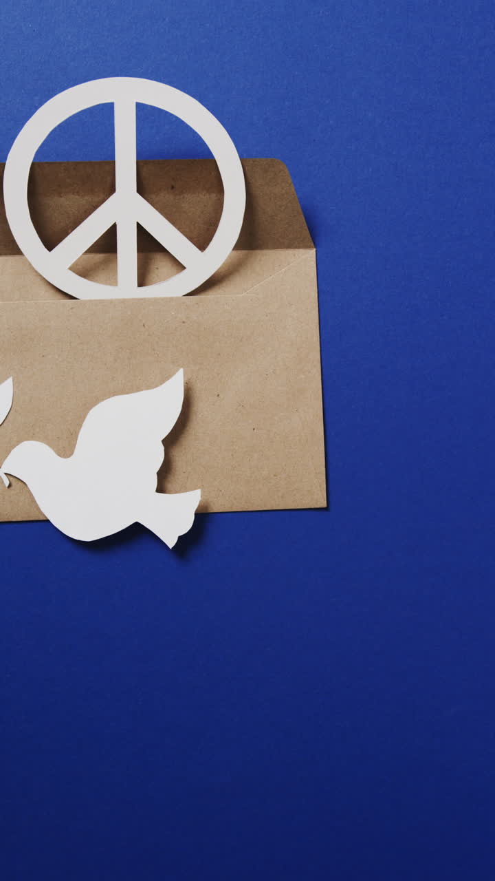Vertical video of white dove with leaf, white peace sign, envelope and copy space on blue background