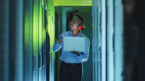 técnico informático afroamericano que usa una computadora portátil trabajando en una sala de servidores de negocios
