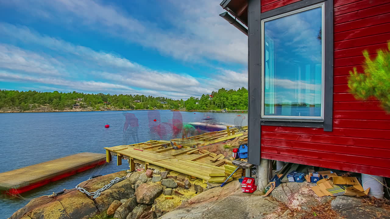 Time lapse of two people building a wooden porch in front of a rustic lake house