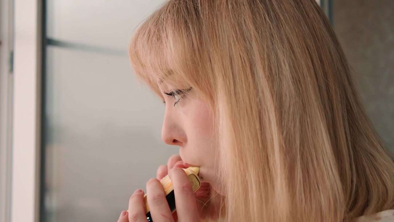 Blonde caucasian woman tasting banana window. Home cook sampling snack, food blogger testing recipe, recipe developer pausing to reflect, nutritionist checking texture, student observing flavor. Soft