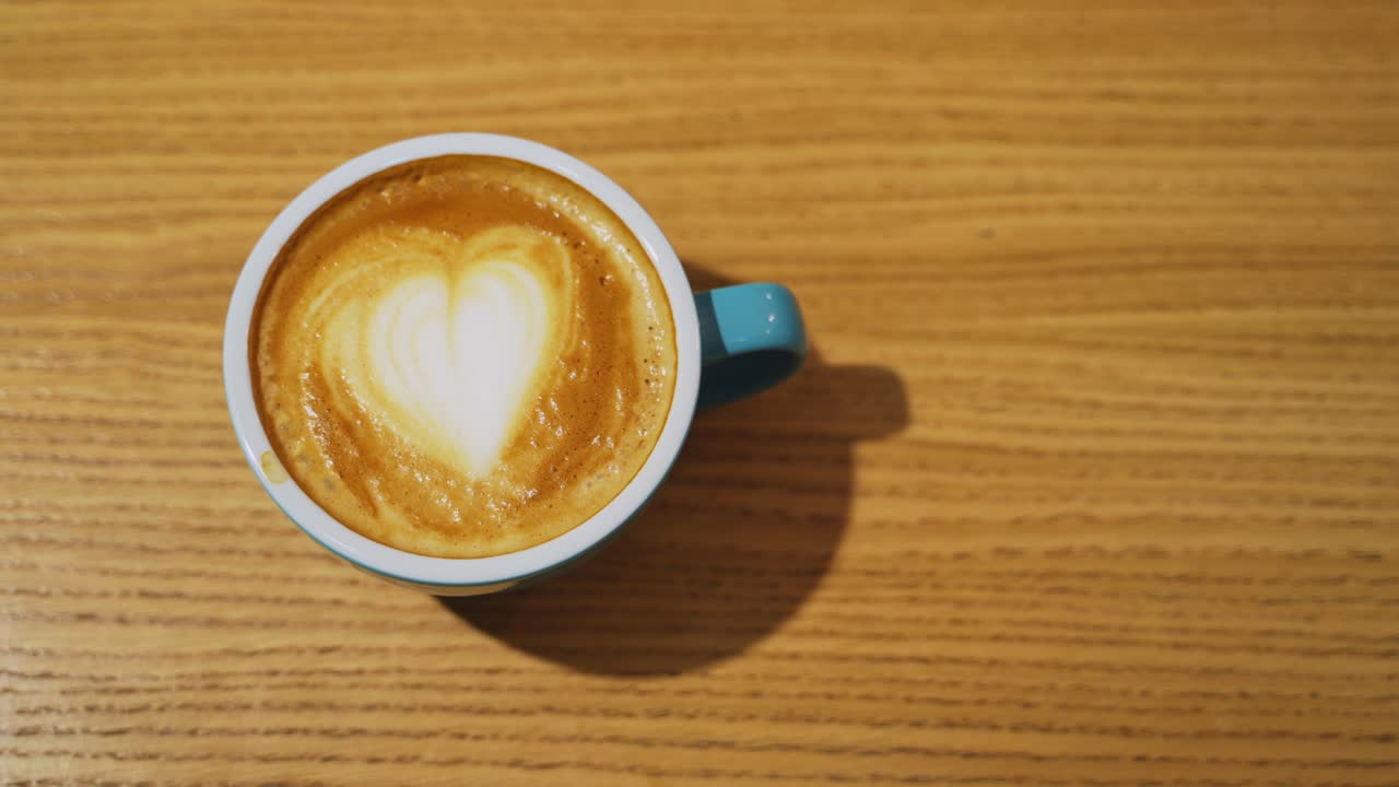 Serving a cup of hot drink. Heart design from milk on coffee. Cup of coffee with latte art in a form of a heart on a wooden background. Close-up.