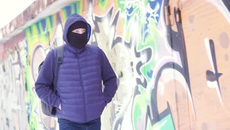 hombre con capucha y máscara cerca de una pared de graffiti