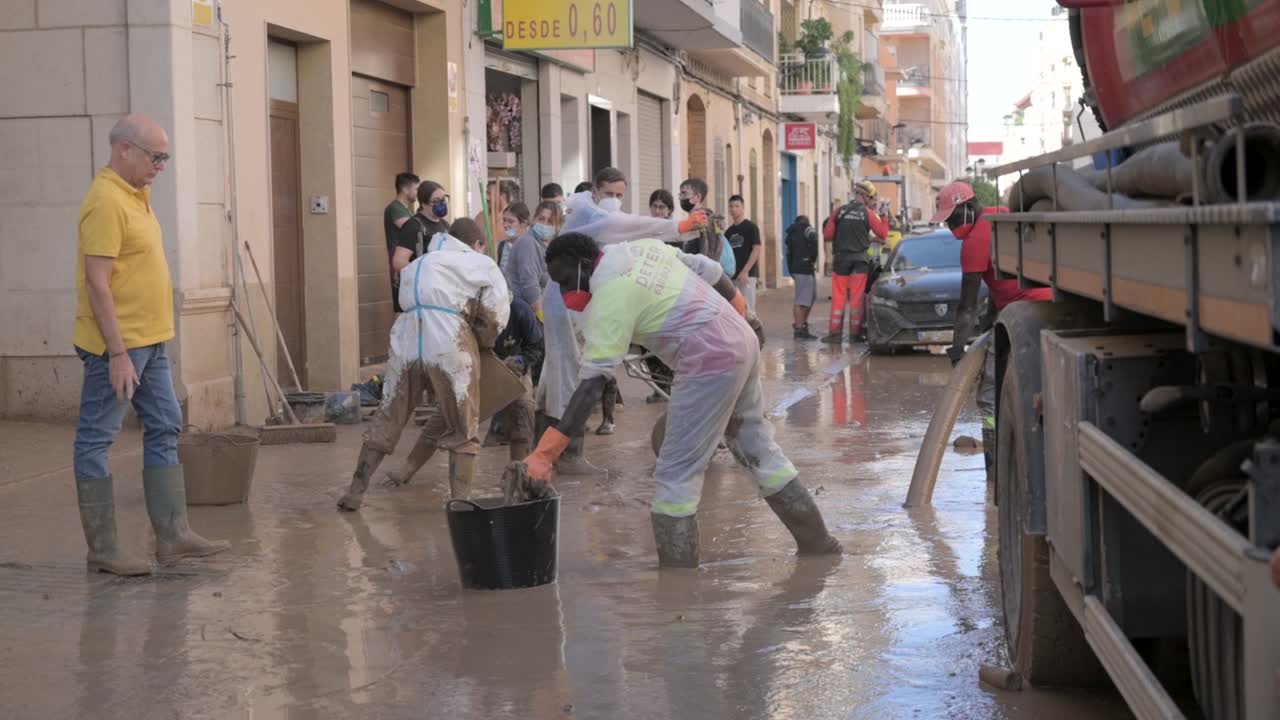 A group of volunteers wearing protective gear clean a muddy street after a severe DANA storm in Valencia