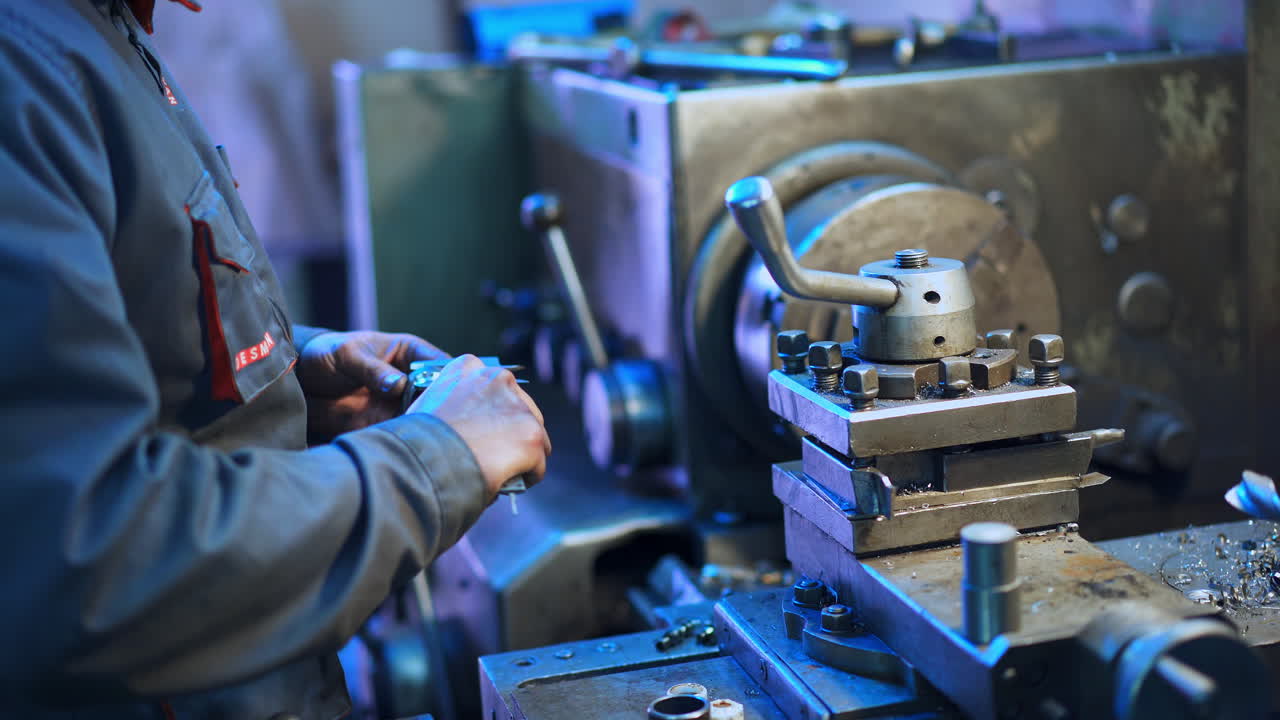 Turner in the uniform standing at his workplace. Man holding a metal detail and examining it. Turner's workshop background.