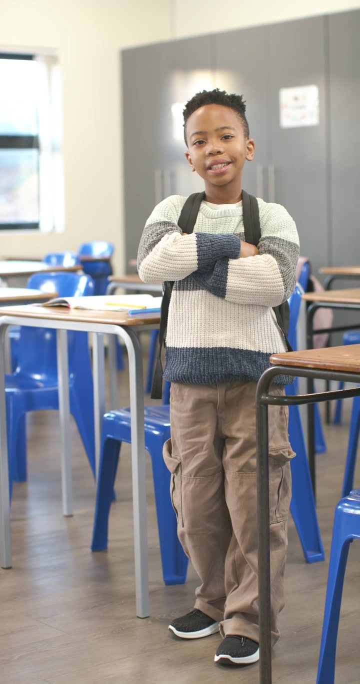 Video verticale: Scolaro che vede la telecamera, sistema il maglione e lo zaino, posa a braccia incrociate in classe