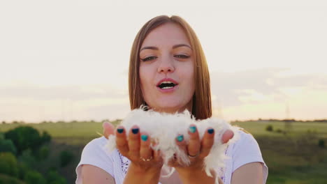 a young woman is playing with a gentle light down blows on a pile of feathers they fly in all direct