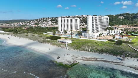 Eine-Filmische-Luftaufnahme-Eines-Pferdes-Am-Strand-Von-Son-Bou-Mit-Gebäuden-Im-Hintergrund-Auf-Menorca,-Spanien