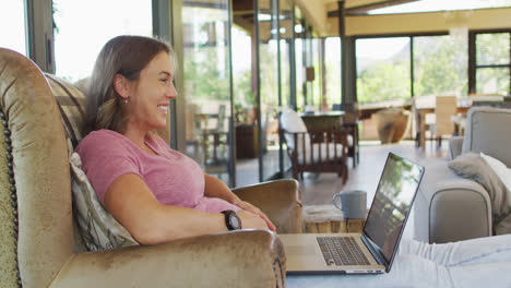 Happy-caucasian-pregnant-woman-sitting-in-armchair,-watching-something-funny-on-laptop