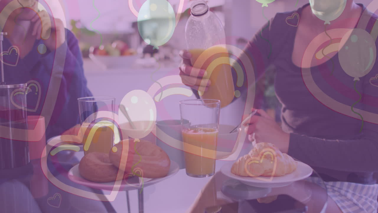 animación de corazones y globos sobre una pareja de mujeres caucásicas desayunando