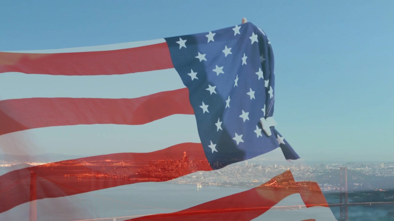 Steady breeze lifting US flag, unfolding stripes and flattening canton revealing skyline and bridge