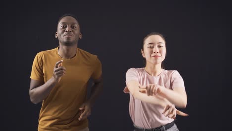 asian young woman and african young man dancing and having fun together. interracial friends.