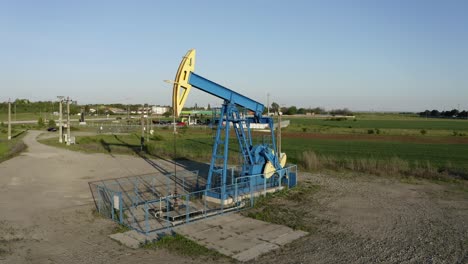 Crane-boom-shot-moving-down-oil-pumpjack-working-near-Ploiesti,-Romania