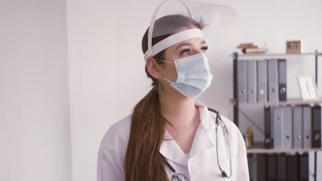 redhead doctor woman in white coat wearing medical mask and facial screen protection