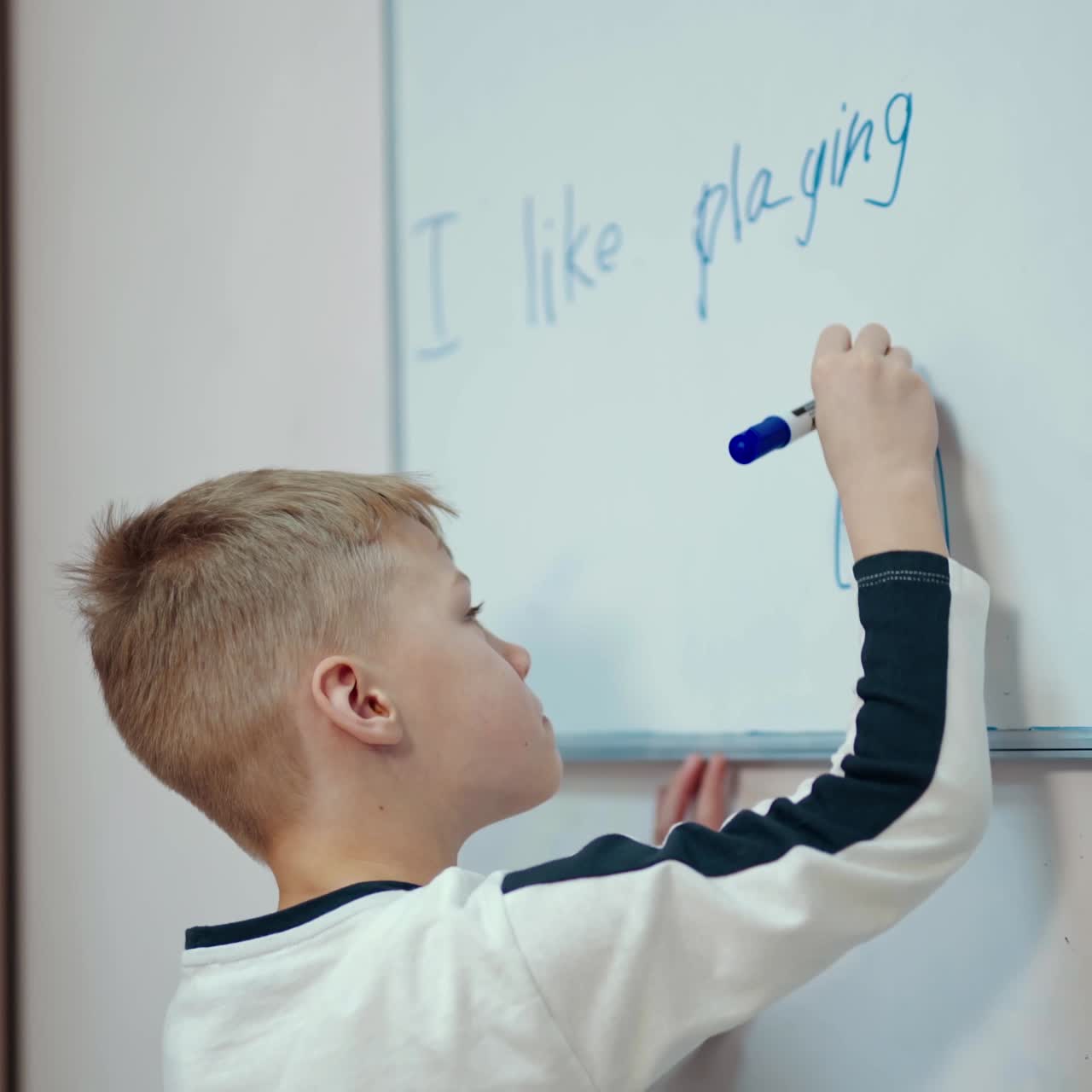 Schoolboy near the whiteboard. Happy boy drawing with a marker on a board in the classroom. Primary pupil at school.