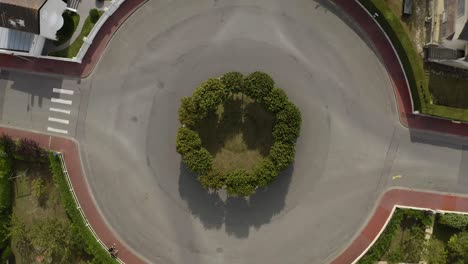 top shot aerial view of traffic roundabout, traffic circle with green trees orange sidewalks and green grass above french typical houses in deauville, france. white muscle sport car passing by 4k uhd.